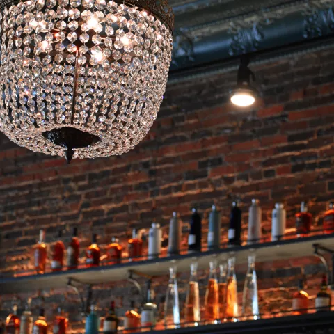 a chandelier hangs in front of exposed brick walls and bar shelves